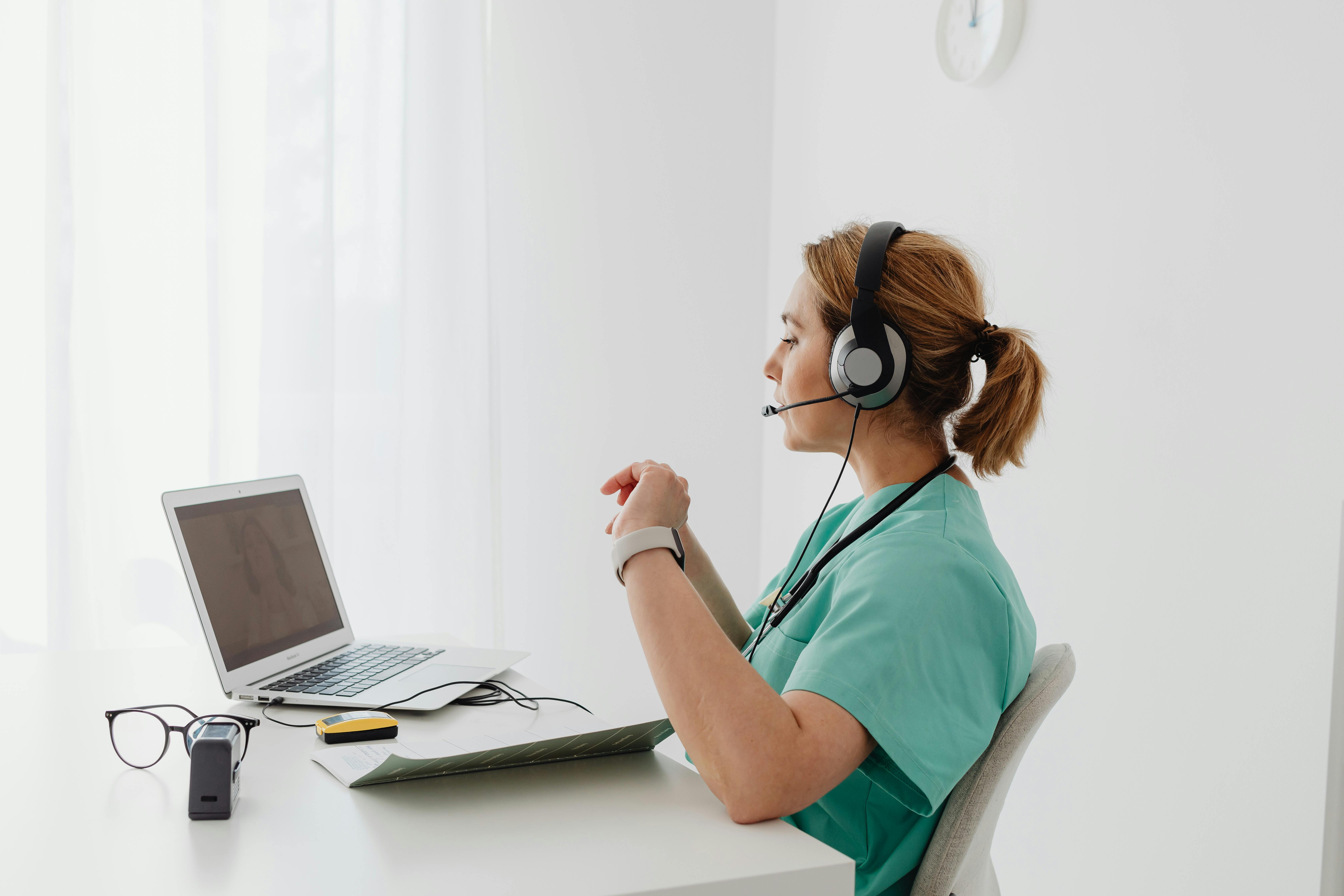 pexels-photo-7195310-7195310 A female doctor using a laptop for an online consultation, wearing a headset in a bright office.