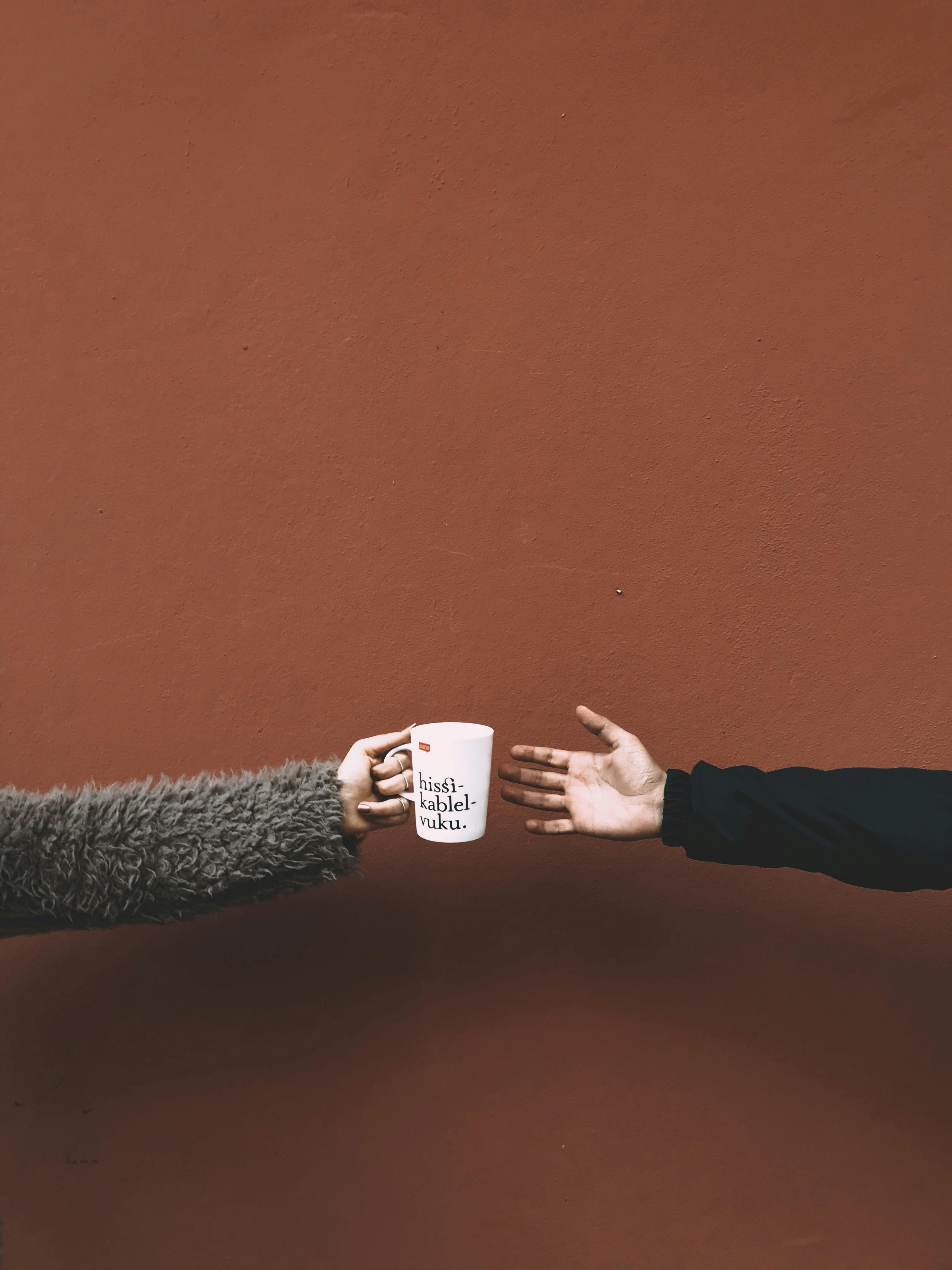 A ceramic mug being handed between two people against a red backdrop, showcasing minimalist style.